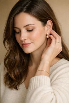 Woman with long brown hair wearing a cream sweater and pearl earrings