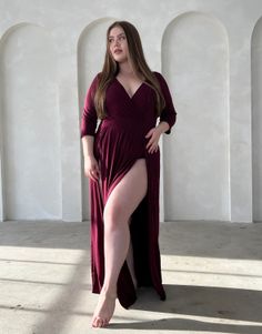 Woman in a long burgundy dress with a high slit and cleavage in an indoor setting