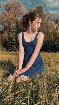 Woman in a blue dress kneeling in a grassy field outdoors
