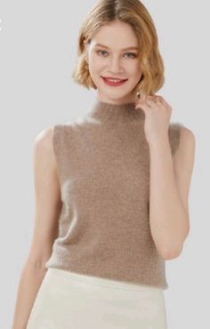 Woman with short blonde hair wearing a brown sleeveless turtleneck top and white pants