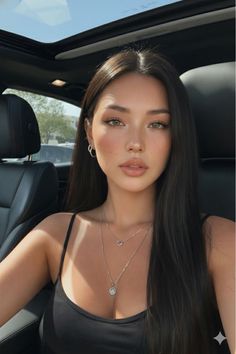 Woman with long dark hair wearing a black top and layered necklaces in a car