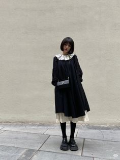 Woman in a black dress with a white collar and glasses standing outdoors