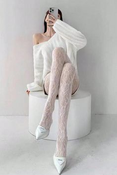 Woman in a white off-shoulder sweater and lace tights taking a mirror selfie