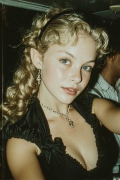 Woman with elf ears and blonde curly hair wearing a black dress and jewelry
