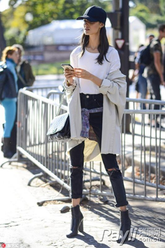 Woman in a black baseball cap, ripped jeans, and a long coat on a street