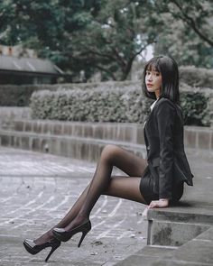 Woman in a black blazer and tights sitting outdoors