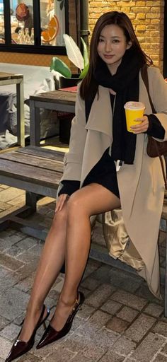 Woman in a trench coat and mini dress sitting outdoors at night