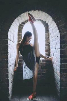 Woman in a black dress and red sneakers doing a high kick in an archway