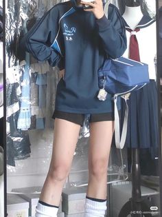 Person in a blue jacket and black shorts with a blue bag, standing indoors