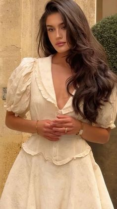 Woman with long dark hair wearing a white dress with puffy sleeves and a ruffle collar