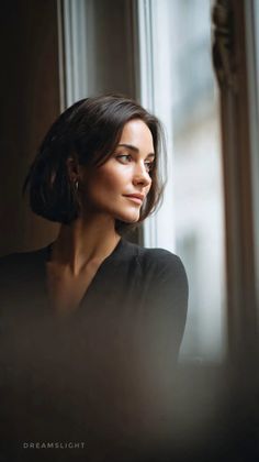 Woman with short dark hair looking out a window with soft lighting