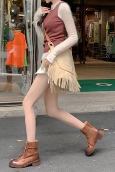 Person in a fringe skirt and brown boots walking on a street