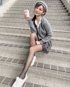 Woman in a beret and cardigan sitting on outdoor stairs, holding a cup