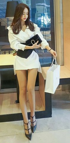 Woman in a white shirt dress and black corset belt holding a clutch bag and shopping bag