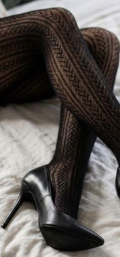 Legs in black patterned tights and high heels on a light surface