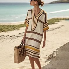 Woman in a striped beach dress and sunglasses holding a straw bag on a sandy beach