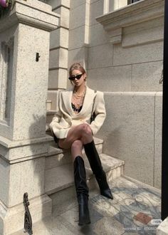 Woman in a blazer and black boots sitting on stone steps outdoors