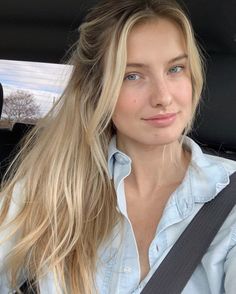 Blonde woman with blue eyes wearing a denim shirt in a car