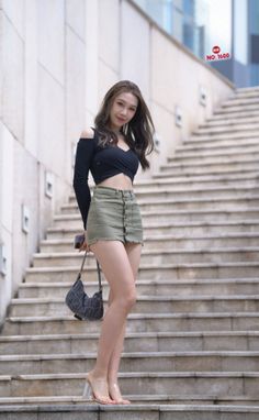 Woman in a black crop top and olive mini skirt standing on outdoor stairs