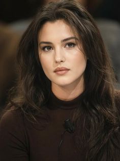 Woman with long brown hair wearing a dark turtleneck, looking directly at the camera