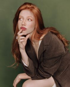 Woman with red hair and freckles wearing a brown jacket against a green background