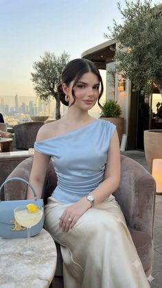 Woman in an off-shoulder top and skirt at a rooftop bar with a cityscape view