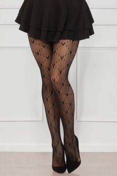 Person wearing black fishnet tights with heart patterns and a black skirt