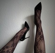 Two legs in lace stockings and black high heels against a white wall