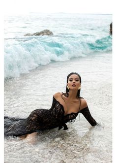 Woman in a black lace dress lying in shallow ocean water with waves