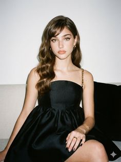 Woman with long wavy hair wearing a black dress and gold jewelry indoors