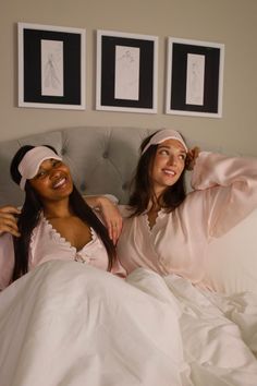 Two women in pink pajamas and sleep masks sitting in bed