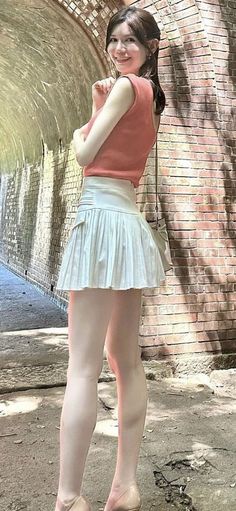 Woman in a pleated skirt and sleeveless top smiling in an outdoor setting