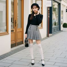 Woman in a plaid skirt, beret, and thigh-high socks standing on a street
