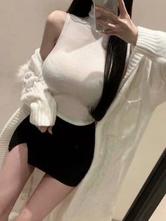 Woman in a white ribbed top and black mini skirt taking a mirror selfie