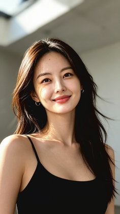 Woman with long dark hair and a black top smiling in soft sunlight