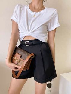 Woman in a white knotted t-shirt and black shorts holding a brown handbag