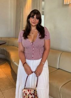 Woman in a red gingham top and white skirt holding a cherry print bag indoors