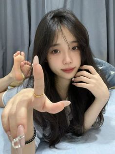 Woman with long dark hair lying on a bed, extending her hand towards the viewer