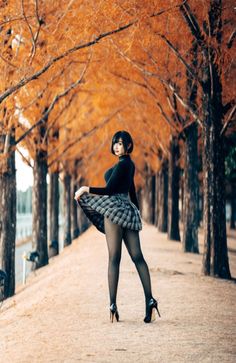 Woman in a plaid skirt and black tights posing outdoors among autumn trees
