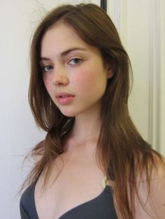 Young woman with long brown hair and blue eyes wearing a dark swimsuit