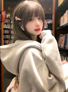 Young woman in a grey hoodie with long hair and bangs in a library