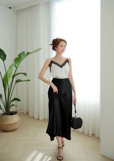 Woman in a lace camisole and black skirt holding a round handbag indoors