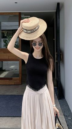 Woman in a black top and pleated skirt holding a straw hat outdoors