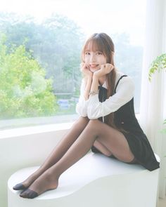 Woman in a black dress and white shirt sitting by a window