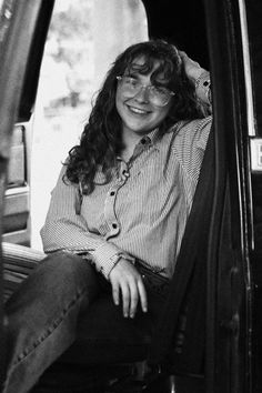 Smiling woman with long hair and glasses in a striped shirt, sitting in a car