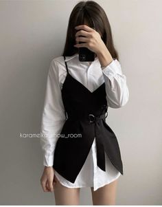 Person in a white shirt and black belted top taking a mirror selfie