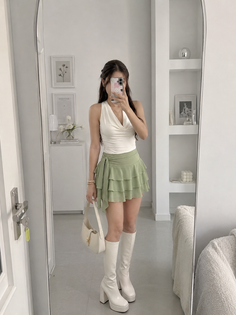 Woman in a white halter top and green ruffled skirt taking a mirror selfie