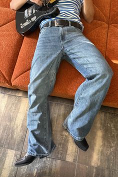 Person playing an electric guitar while lying on an orange couch