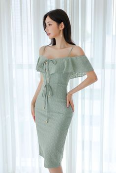 Woman in a light green off-shoulder dress with pearl earrings standing indoors