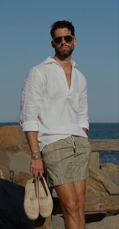 Man in a white shirt and sunglasses holding espadrilles at the beach
